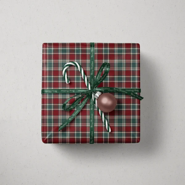 Top view of a gift in burgundy and green tartan paper with a ribbon, candy canes and a bauble
