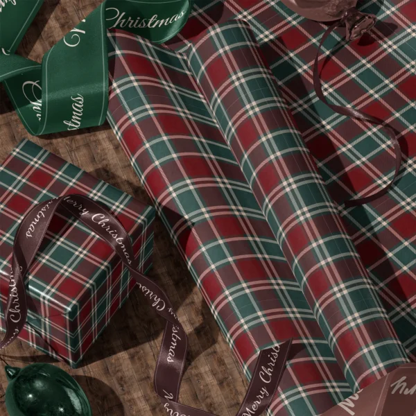 Rolls of burgundy and green tartan gift wrap and a wrapped box with satin ribbons on a wooden floor