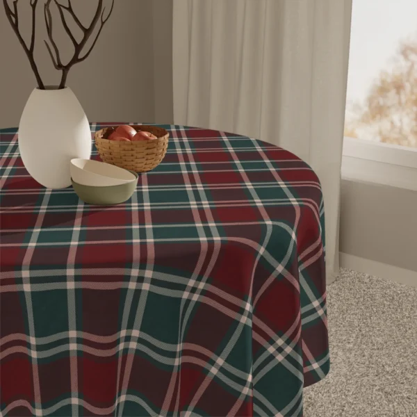 Close-up of a dark red and green plaid tablecloth with a white vase, a small bowl and a basket of apples