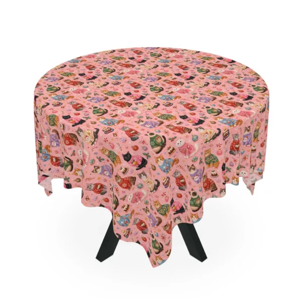 Pink tablecloth on a round table printed with cats in colorful holiday sweaters, candy canes and puddings
