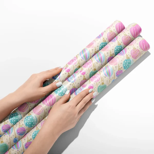 Hands smoothing three rolls of cream pastel ornament wrapping paper on a white table