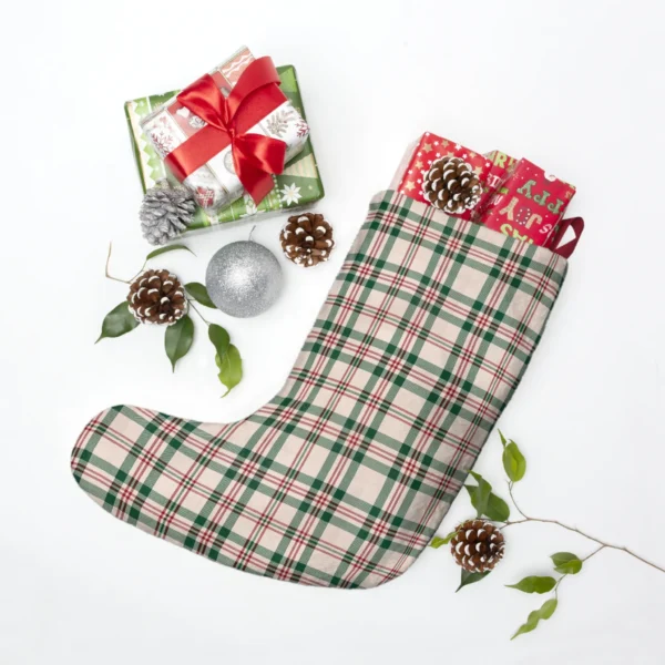 Cream tartan stocking filled with red gift boxes, lying beside pine cones, holly leaves and a silver bauble