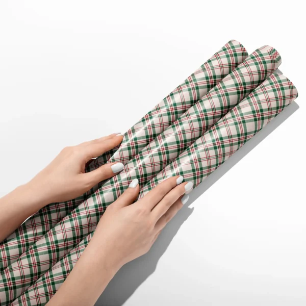 Hands smoothing three rolls of cream plaid wrapping paper on a white table