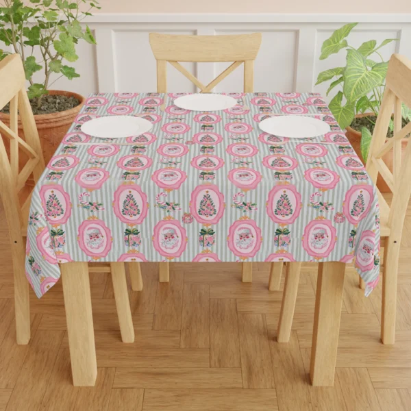 Dining table laid with white plates on a pink and sage Santa tablecloth, wooden chairs and green plants around it
