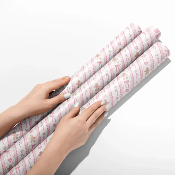 Hands smoothing three rolls of pink gingerbread wrapping paper on a white table