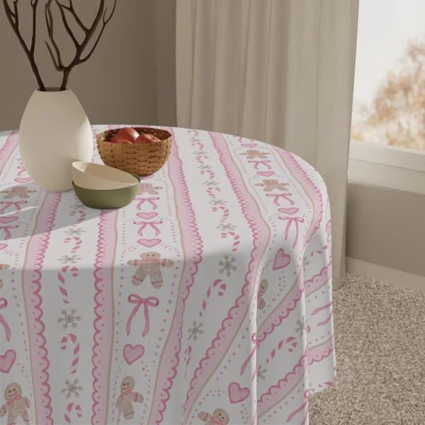 Close view of pink bows and gingerbread figures on a tablecloth beside a white vase and a basket of apples