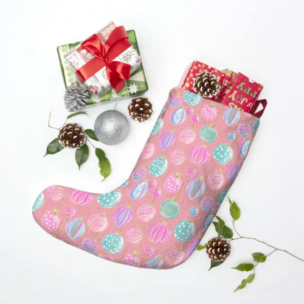 Pink pastel bauble stocking laid flat among wrapped presents, pine cones and a silver ornament