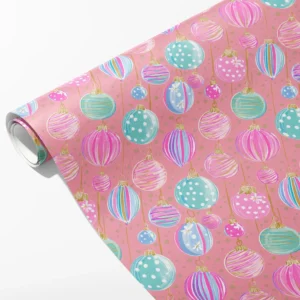 Roll of pink wrapping paper with pastel pink, teal and lilac Christmas ornaments, partly unrolled on white