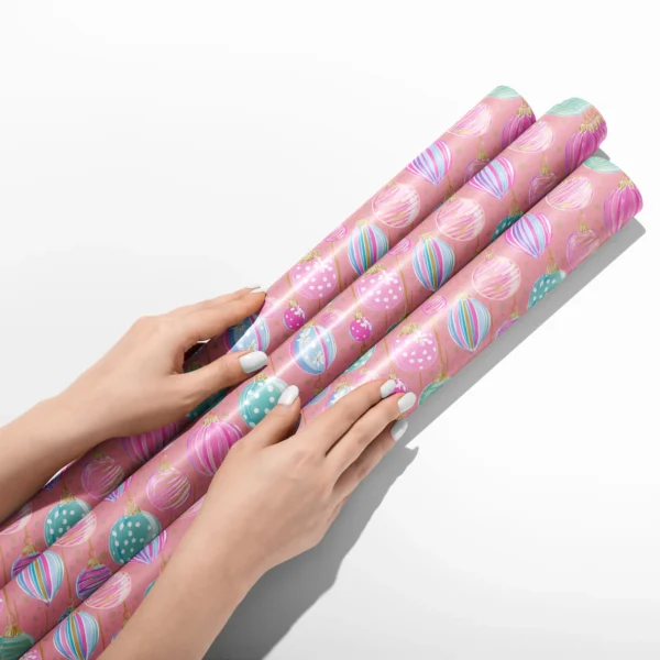 Hands smoothing three rolls of pink pastel ornament wrapping paper on a white table