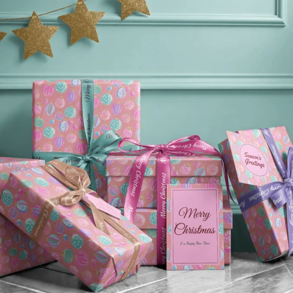 Stack of presents in pink pastel ornament paper with ribbons and a Merry Christmas card by a teal wall