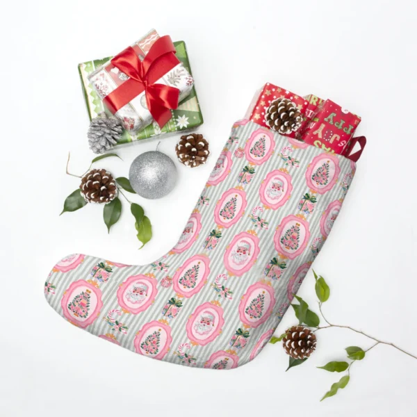 Pink and sage Santa stocking laid flat among wrapped presents, pine cones and a silver bauble