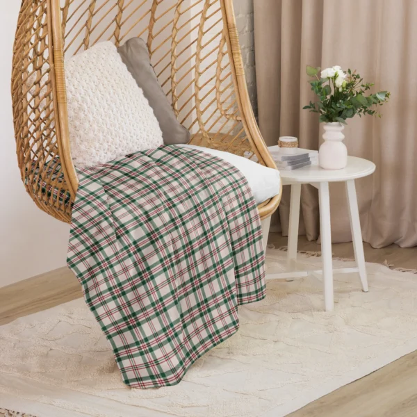 Cream plaid Christmas throw draped over a rattan hanging chair beside a white side table and flowers