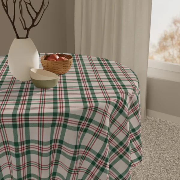 Close view of a green and red check tablecloth with a white vase, bowls and a basket of apples