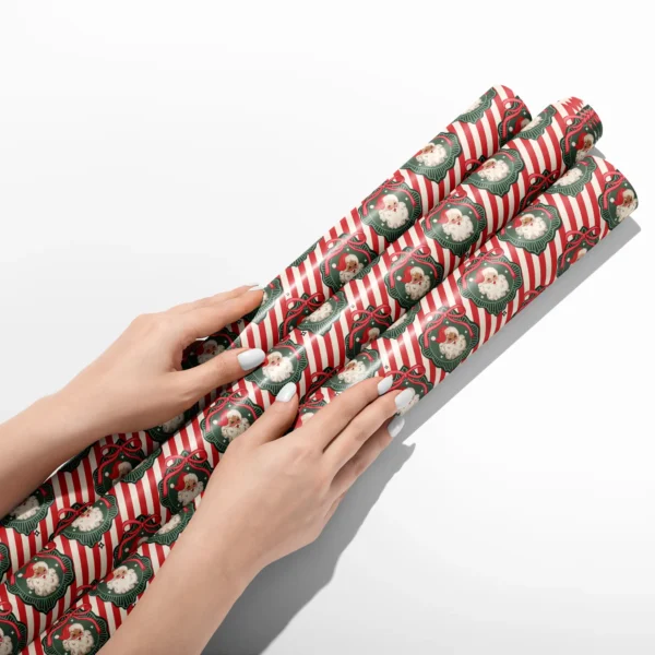 Hands smoothing three rolls of vintage Santa red stripe wrapping paper on a white table