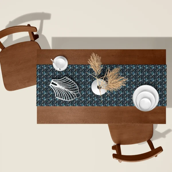 Blue snowflake Christmas table runner seen from above on a walnut table with white dishes and dried pampas