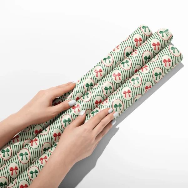 Hands smoothing three rolls of bow medallion wrapping paper on a white table