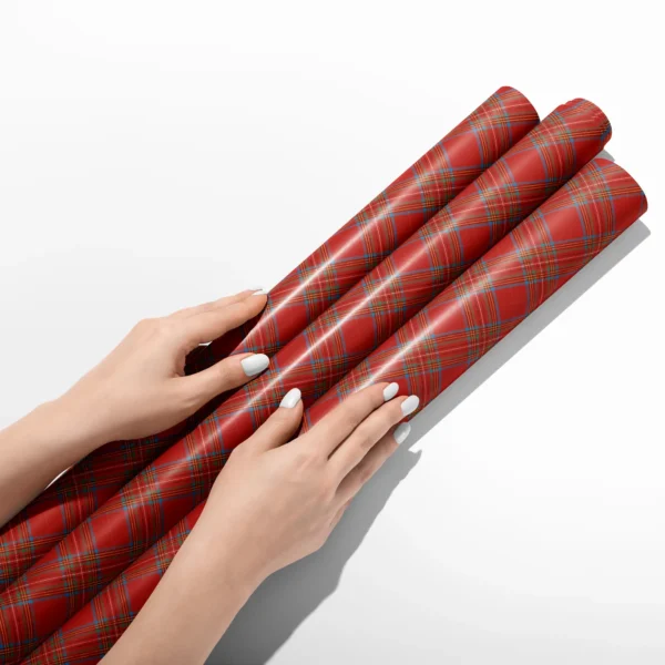 Hands smoothing three rolls of red tartan wrapping paper on a white table