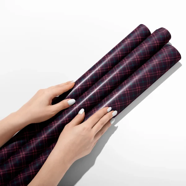 Hands smoothing three rolls of burgundy houndstooth plaid wrapping paper on a white table