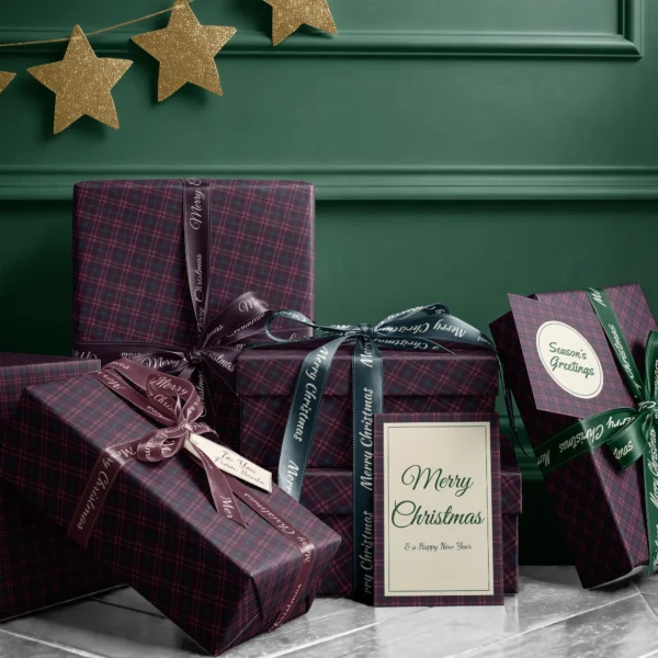 Stack of presents in burgundy houndstooth plaid paper with ribbons and a greeting card by a dark green wall