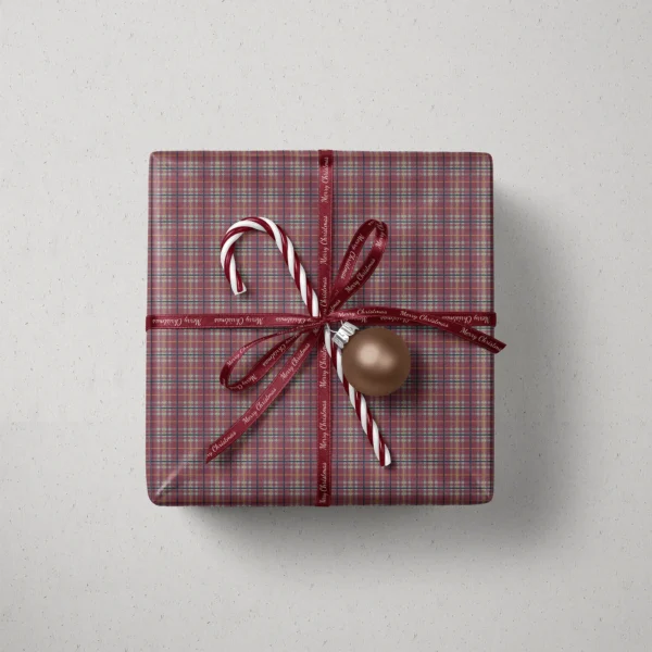 Top view of a gift in burgundy and sage plaid paper with a ribbon, striped candy and a bauble