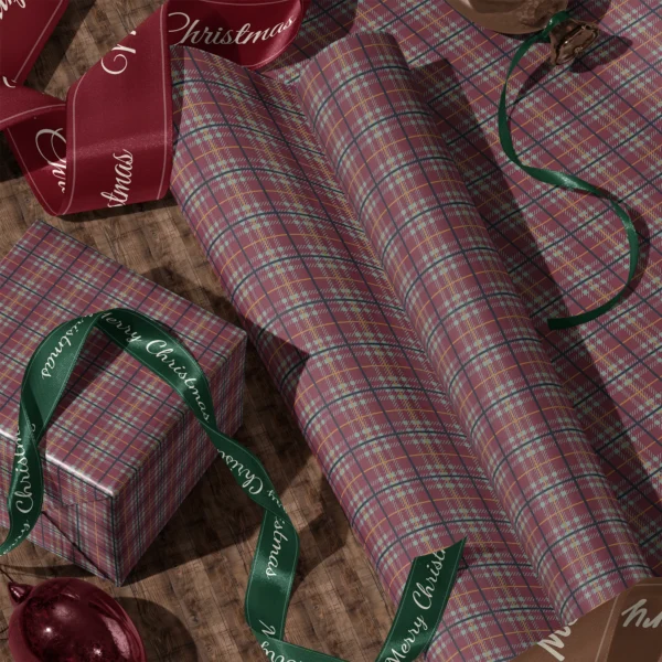 Rolls of burgundy and sage plaid gift wrap and a wrapped box with satin ribbons on a wooden floor