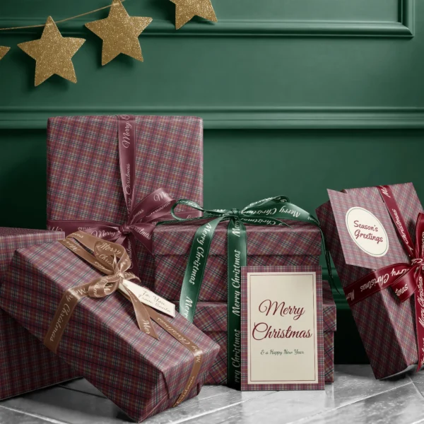 Stack of presents in burgundy and sage plaid paper with ribbons and a greeting card by a dark green wall