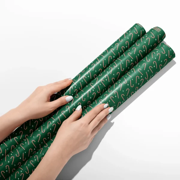 Hands smoothing three rolls of candy cane wrapping paper on a white table