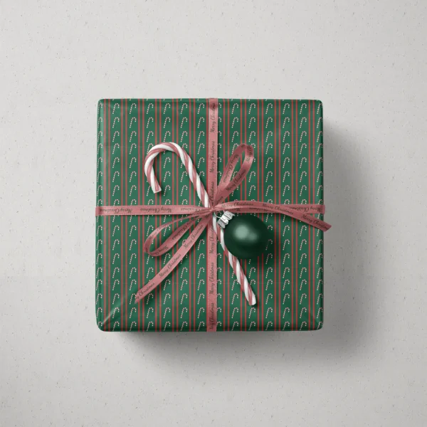 Top view of a gift in candy cane stripe paper with a ribbon, candy canes and a bauble