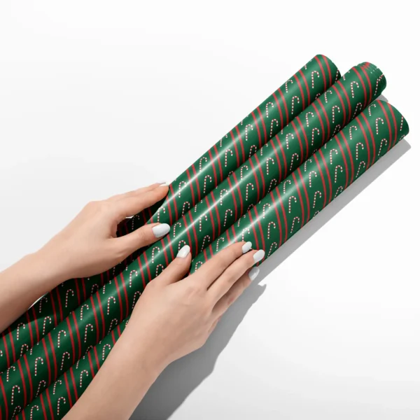 Hands smoothing three rolls of candy cane stripe wrapping paper on a white table