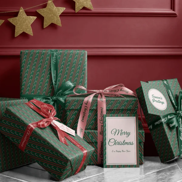 Stack of presents in candy cane stripe paper with ribbons and a Merry Christmas card by a burgundy wall