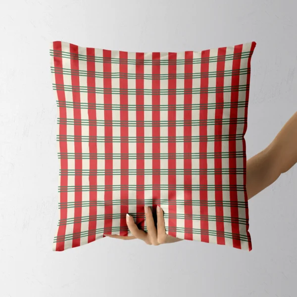 A hand holding the red and cream peppermint plaid throw pillow