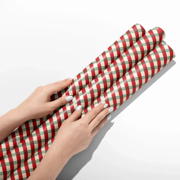 Hands smoothing three rolls of candy stripe plaid wrapping paper on a white table