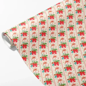 Roll of cream wrapping paper with red bows, pine sprigs and holly in tall columns, partly unrolled on white