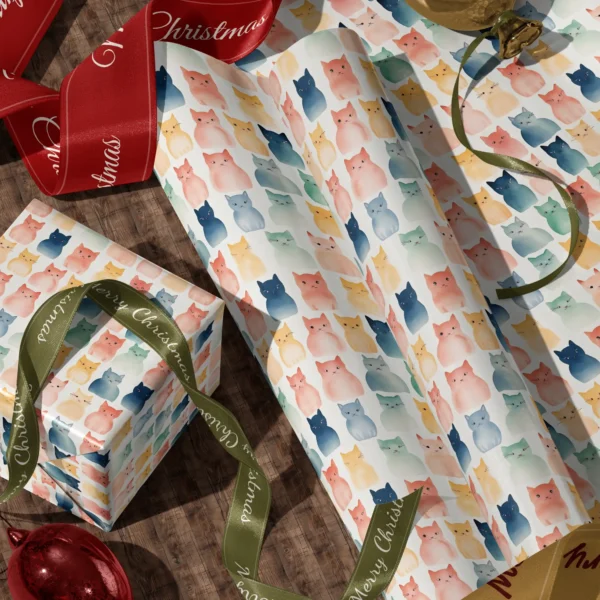 A sheet of cream watercolor cat gift wrap and a wrapped box with red and green satin ribbons on a wooden floor