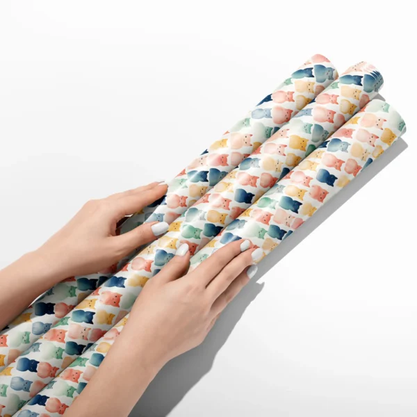 Hands smoothing three rolls of cream watercolor cat wrapping paper on a white table