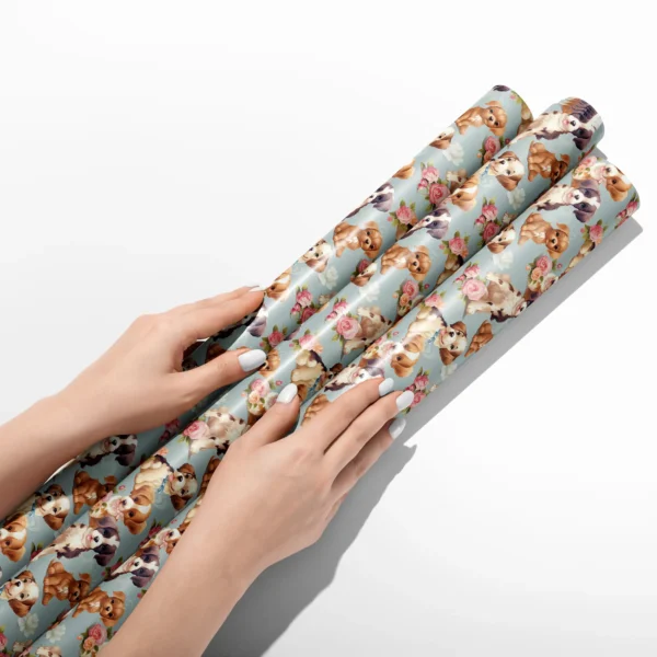 Hands smoothing three rolls of dusty blue puppy and rose wrapping paper on a white table
