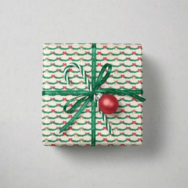 Top view of a gift in pine garland paper with a ribbon, candy canes and a bauble