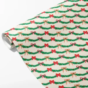 Roll of cream wrapping paper with rows of pine garland swags and red bows, partly unrolled on white