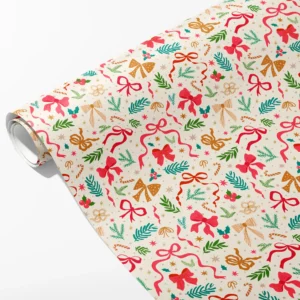 Roll of cream wrapping paper with scattered pink, red and gold bows, pine sprigs and candy canes, partly unrolled on white
