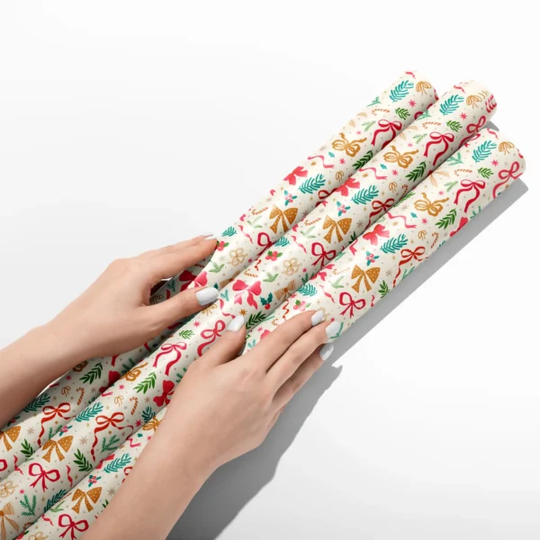 Hands smoothing three rolls of ribbon and greenery wrapping paper on a white table
