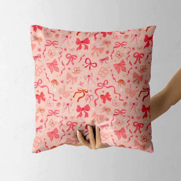 A hand holding the blush pillow printed with pink bows