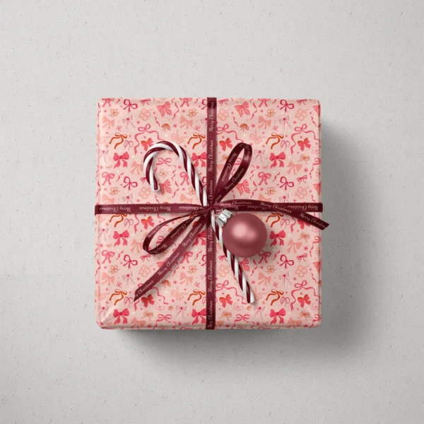 Top view of a gift in coquette bow paper with a ribbon, candy canes and a bauble