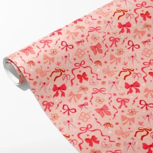 Roll of blush pink wrapping paper with scattered pink, red and plaid bows and small stars, partly unrolled on white