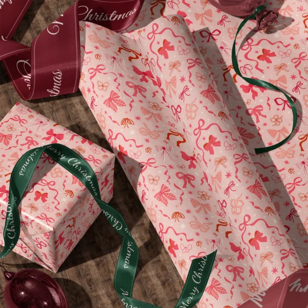Rolls of coquette bow gift wrap and a wrapped box with satin ribbons on a wooden floor