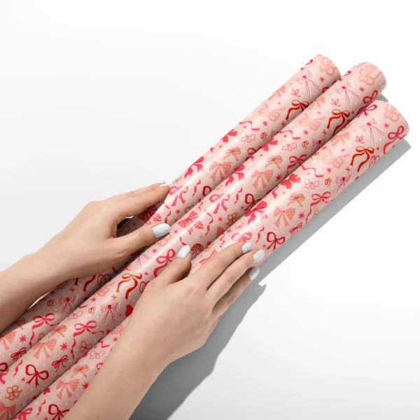 Hands smoothing three rolls of coquette bow wrapping paper on a white table