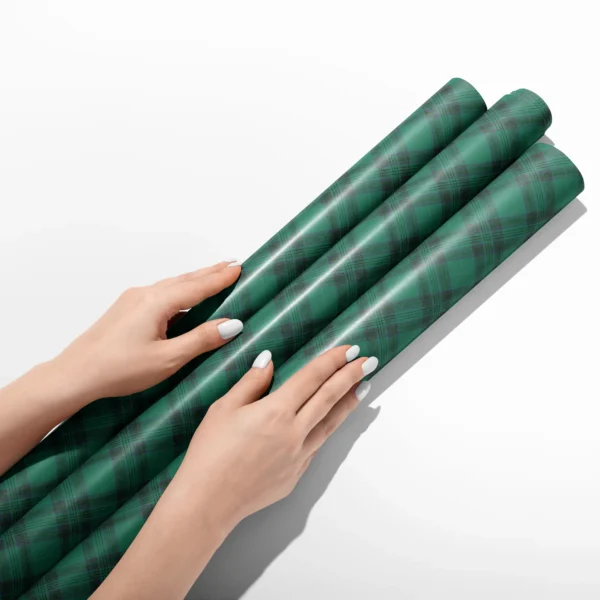 Hands smoothing three rolls of emerald green tartan wrapping paper on a white table