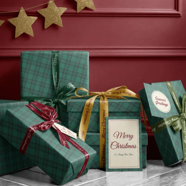 Stack of presents in emerald green tartan paper with ribbons and a Merry Christmas card by a burgundy wall