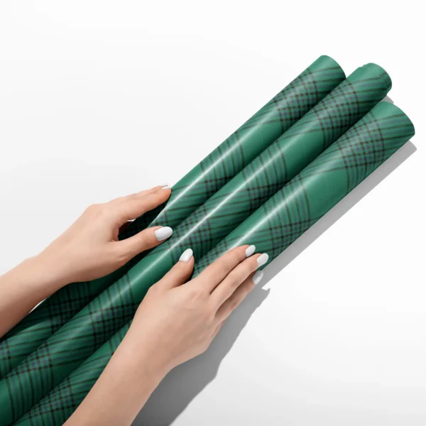 Hands smoothing three rolls of emerald windowpane plaid wrapping paper on a white table