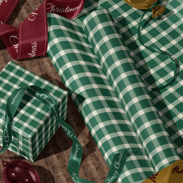 Rolls of evergreen gingham gift wrap and a wrapped box with satin ribbons on a wooden floor