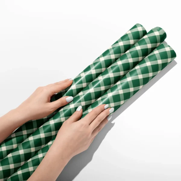Hands smoothing three rolls of evergreen gingham wrapping paper on a white table